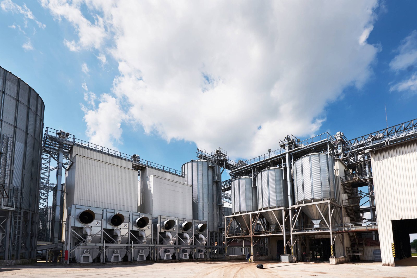 Agricultural Silos. Building Exterior. Storage and drying of grains, wheat, corn, soy, sunflower against the blue sky with white clouds.